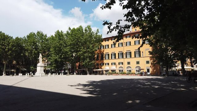 Steadicam shot of Square Piazza Napoleone in Lucca, Italy with large trees and statue 