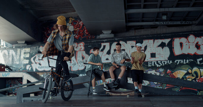 Sporty Man Performing Jump Trick On Bmx Bike At Skate Park With Graffiti. 