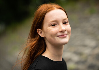 Red haired twelve year old girl with freckles posing with a nature bokeh background