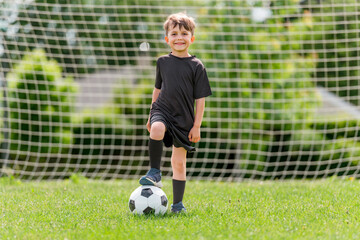 Cute boy playing football enjoying sport game outside - Powered by Adobe