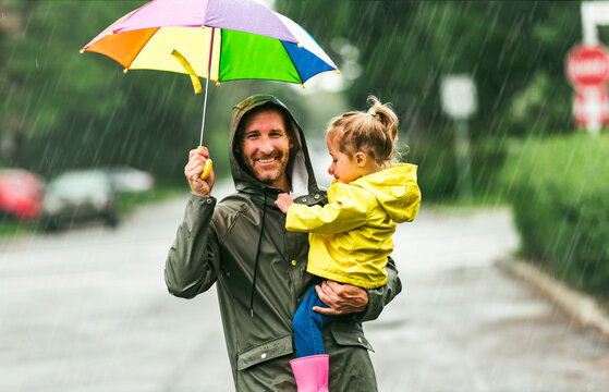 Happy funny father holding multicolored umbrella under the summer raining day with the child girl