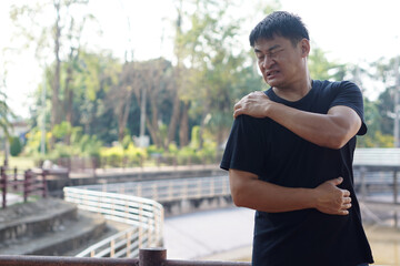 Portrait of Asian man stands outdoor, feels hurt his shoulder. Concept : Health problems, swelling...