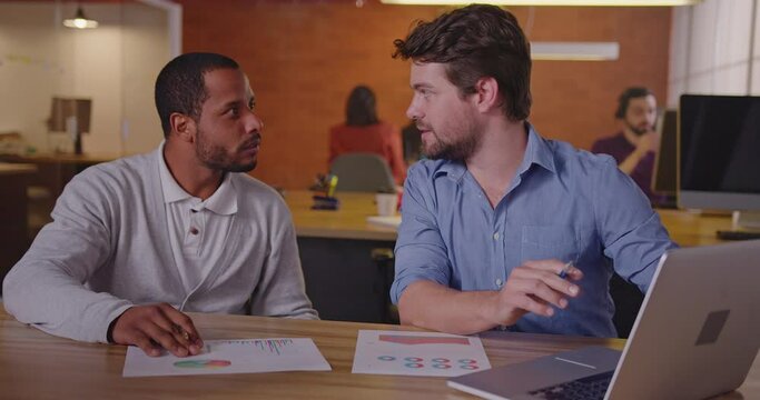 Two office colleagues at meeting looking at laptop computer together. A black man listening to information protocol at First day at new job concept