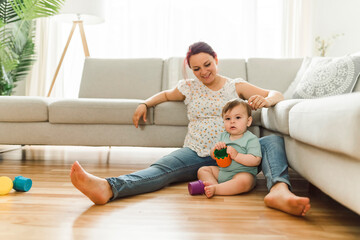 Mother and the Cute 8 month baby laying on floor, playing with toys