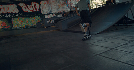 Active scooter rider performing tricks during freestyle session at skate park.