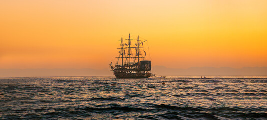 Enchanted Spanish Galleon pirate ship storybook magic sailing into sunset. Pirate ship sailing on the ocean at sunset.