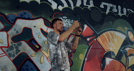 Young man shooting video on mobile phone for blog at skate park with graffiti. © stockbusters