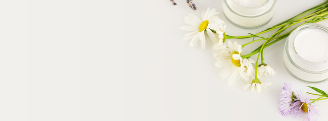 Natural cosmetic banner with organic creams and wild flowers on a white background with copy space. Concept of wild-harvested beauty and natural cosmetics based on a wild plant. Soft focus style