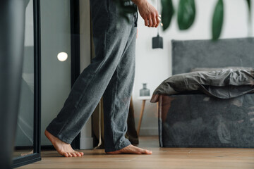 Young white man in gray pants walking through bedroom at home