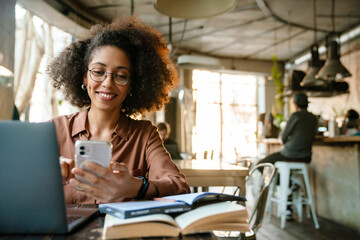 Young african american woman using cellphone while working in cafe