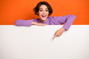 Photo of charming positive girl direct finger empty space proposition blank isolated on orange color background