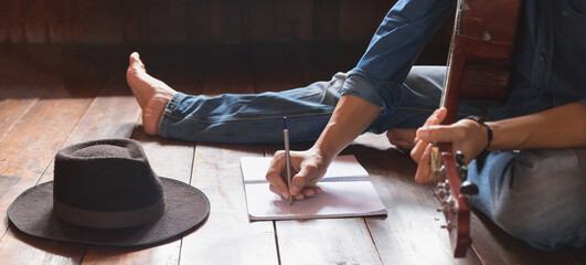 Musicians with acoustic guitars and hipster hats sitting writing songs on paper on a wooden floor...