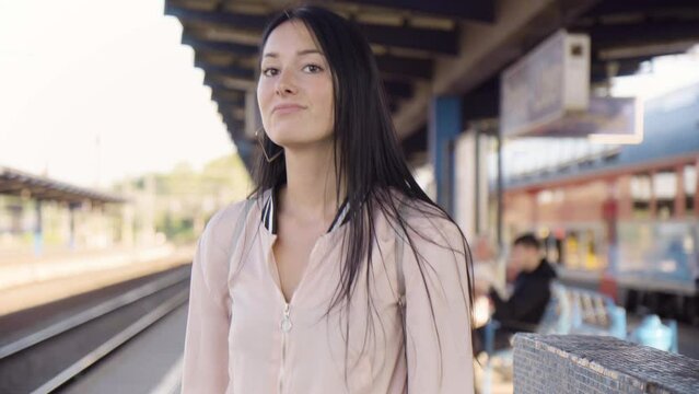 A young beautiful Caucasian woman is frustrated as she waits impatiently for a train at a train station - closeup