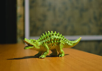 A figurine of a green dinosaur with spikes stands on a brown table