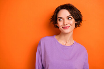Photo of confident dreamy young lady wear violet sweatshirt looking empty space isolated orange color background