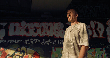 Fototapeta na wymiar Smiling teenager roller skating at skatepark with graffiti wall background. 
