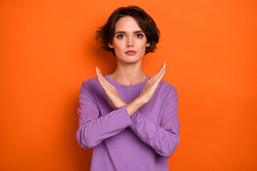 Portrait of confident serious girl crossed arms demonstrate stop gesture isolated on orange color background