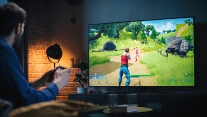 Young Man Spending Time at Home, Sitting on a Couch in Stylish Loft Apartment and Playing Arcade...