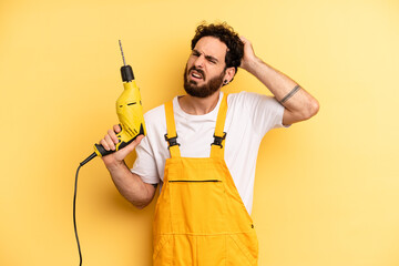 young man smiling happily and daydreaming or doubting. handyman with a drill