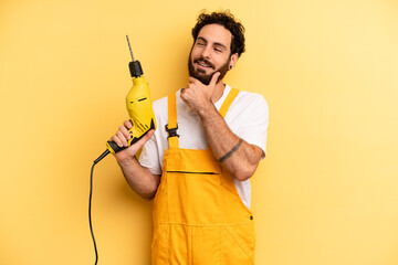 young man smiling with a happy, confident expression with hand on chin. handyman with a drill