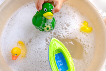 happy child, girl 3 years old plays with rubber green, yellow ducks for swimming, plastic boat, child's toys in soapy foam, concept bathing in bathtub, playing with water, hygiene, healthy lifestyle