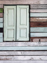 Old grunged wooden window frame painted white vintage with old colourful plywood wall. Antique window frame and old panes. Old closed window and planks of old wooden house. Background of wooden walls