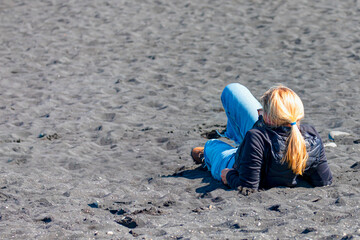 A blond woman is resting on the black sand beach - Diamond Beach Near Jokulsarlon Glacier Lagoon  iceland