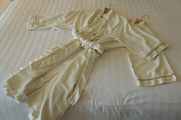 Close-up of two light cream robes on the bed In the hotel room.   Terry cloth bathrobe on two hangers stacked on white bedding. It is commonly worn over after a shower or when going to spa or swimming