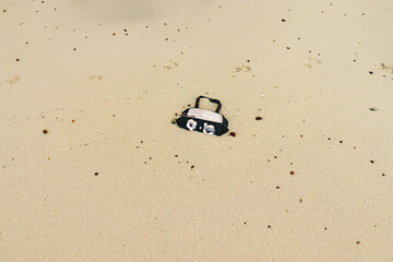 A discarded plastic purse washed up and half buried on the sand