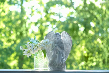 Praying angel and white flowers on table, abstract natural green background. Religious holiday....