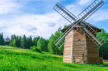 Fototapeta na wymiar Wooden windmill for grinding flour. An old wooden windmill built in the 19th century. A mill for grain processing and flour production against the background of a green forest and a blue sky.