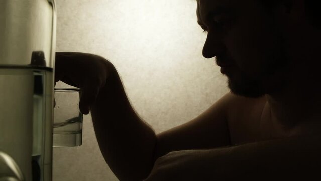 Alcoholic man drinking vodka sitting at a table with bottles, silhouette video.