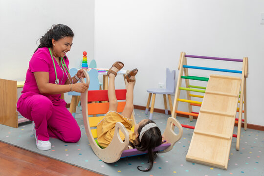 Latina pediatric doctor, laughing while playing with a girl in the play area of her office