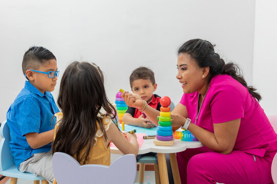 Female pediatrician sitting at a table with several children playing in her medical office