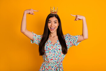Photo of adorable young selfish female pointing at her beautiful crown on head isolated on yellow...