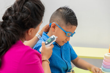 Pediatrician checking the temperature of a child with glasses, in his office