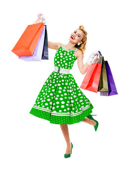 Full body of jumping, running, dancing woman in pinup style green color dress holding, showing shopping bags, isolated on white background. Sales, discounts rebates or consumer bank credit ad concept.