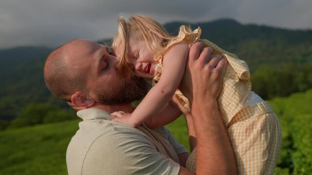 happy childhood and fatherhood, man is kissing his little daughter, portrait of family in nature