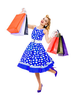 Full body of jumping, running, dancing woman in pinup style blue dress holding, showing shopping bags, isolated on white background. Sales, discounts rebates or consumer bank credit ad concept picture