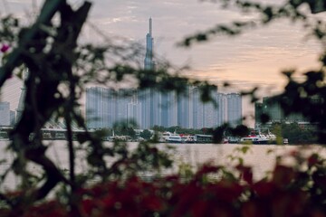 Blurred view of the Landmark 81 on the bank of Saigon River in Vietnam behind tree leaves