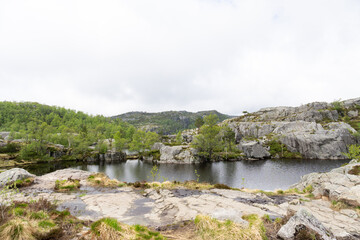 Fototapeta na wymiar Lake surrounded by rocks and trees on a cloudy Norwegian day, on the way to Preikestolen.