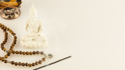 Buddha statue, prayer beads and aroma sticks on a white background with copy space. Asian spa ritual procedure, healing and meditation. Energetic health and relax. Vesak, Buddha Day. Soft image style