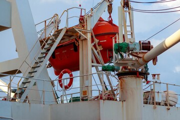 Red lifeboat tanker hanging in the air in a ship in cloudy sky background