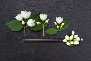 White jasmine flowers and black  spoon on a black slate surface. Top view. Shallow depth of field