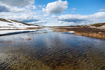 Scenic view of a river flowing in a rural area surrounded by snow in cloudy sky background