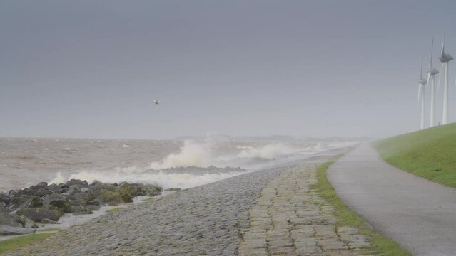 Waves on the IJsselmeer hitting the levee of the Noordoostpolder with a row of wind turbines during an early springtime storm in The Netherlands