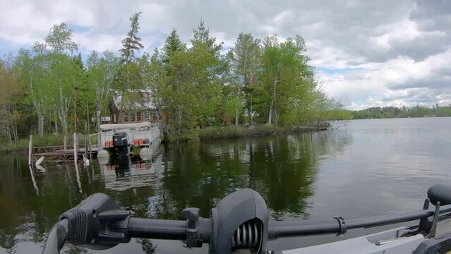POV - Front of fishing boat and trolling motor while slowly cruising by lake home with a pontoon boat on Lake Vermilion in northern Minnesota; lake at flood stage; concepts of fishing and vacation