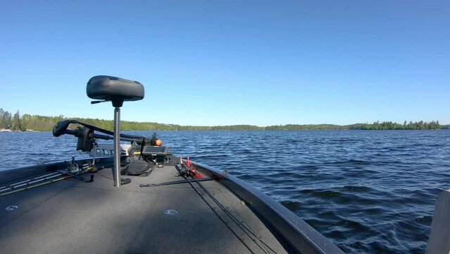 Front end of bass fishing boat with a butt seat, trolling motor and fishing rods; pulling away from dock into open water of Lake Vermilion in  Minnesota; concepts of fishing, calm, and vacation