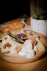variety of cheeses on wooden board accompanied with a piece of bread on a dark background