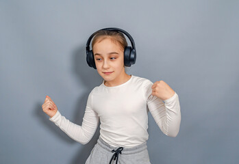 Dancing little girl in headphones listening to music. White T-shirt, gray sweatpants.